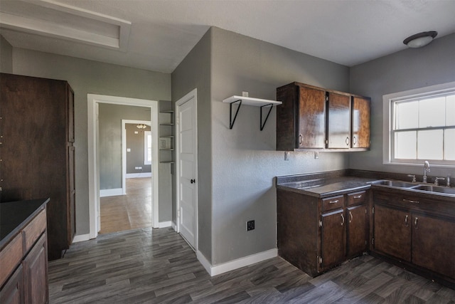 kitchen with dark brown cabinetry, a sink, dark wood-style floors, baseboards, and dark countertops