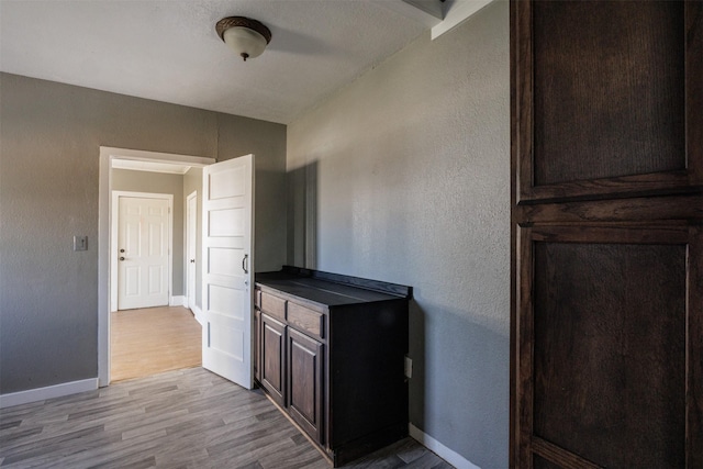 kitchen featuring light wood finished floors, baseboards, dark countertops, dark brown cabinets, and a textured wall