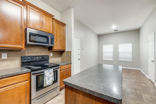 9212 Water Oak Dr, Arlington, TX 76002 - kitchen featuring appliances with stainless steel finishes, dark countertops, decorative backsplash, brown cabinetry, and a center island