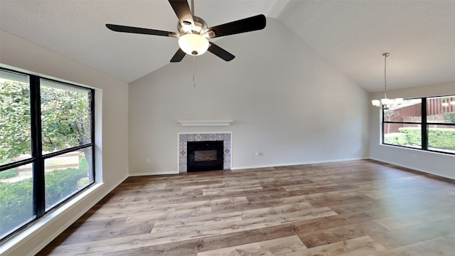 unfurnished living room with high vaulted ceiling, ceiling fan with notable chandelier, baseboards, a tiled fireplace, and light wood-style flooring