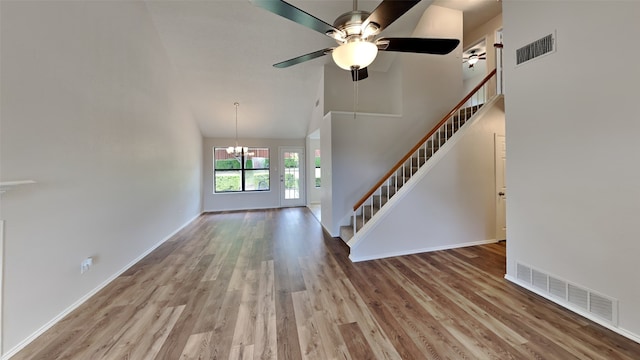 unfurnished living room featuring stairs, visible vents, wood finished floors, and a towering ceiling