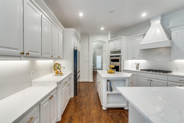 kitchen featuring arched walkways, gas stovetop, high end fridge, custom range hood, and stainless steel double oven