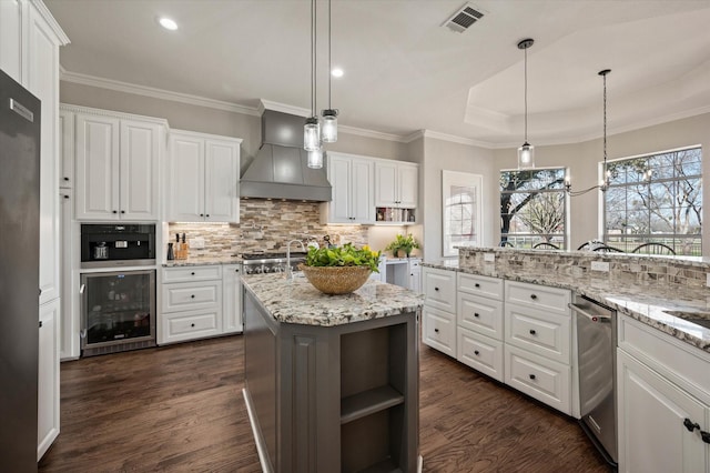 kitchen featuring a tray ceiling, open shelves, wine cooler, visible vents, and wall chimney exhaust hood