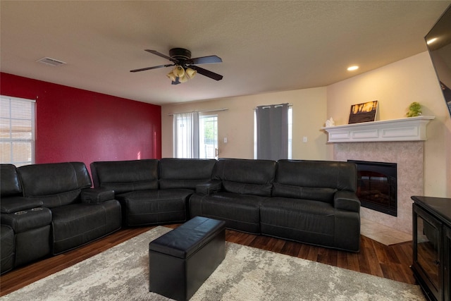 living area featuring ceiling fan, visible vents, a tile fireplace, and wood finished floors