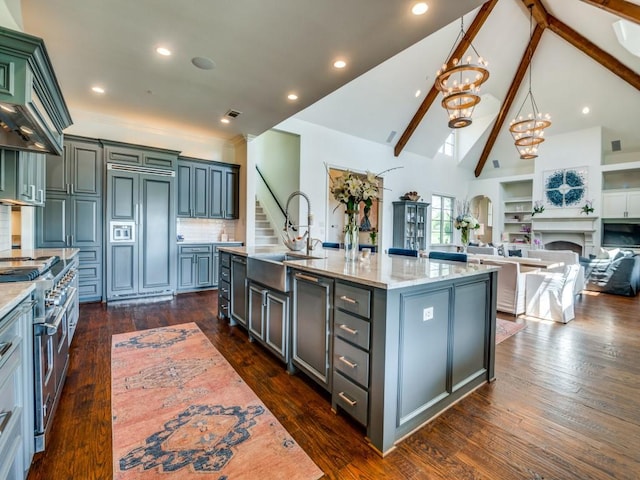 kitchen with high end appliances, open floor plan, a center island with sink, high vaulted ceiling, and a sink
