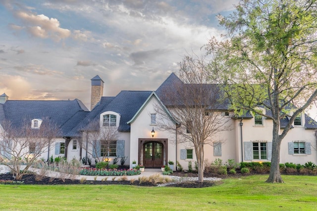 french country home with stucco siding, a chimney, french doors, and a front lawn