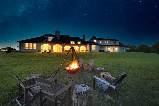 back of house at twilight featuring a lawn, a chimney, and a fire pit