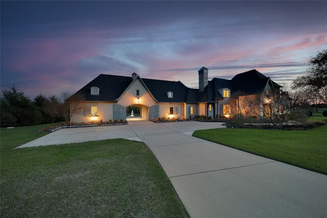 view of front of property featuring curved driveway, a chimney, stucco siding, and a front yard