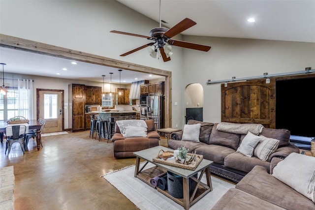 living area with concrete flooring, a barn door, high vaulted ceiling, a ceiling fan, and recessed lighting