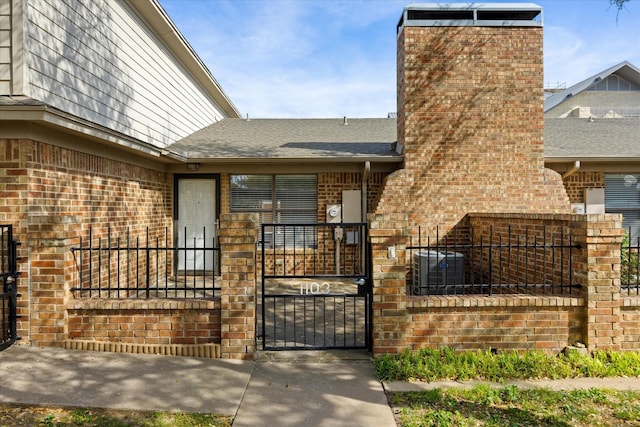 exterior space with brick siding, fence, a gate, and roof with shingles