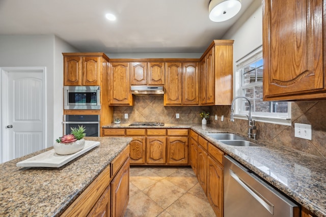 8312 Rancho De La Osa Trl, Mckinney, TX 75070 - kitchen featuring stainless steel appliances, a sink, under cabinet range hood, brown cabinetry, and backsplash