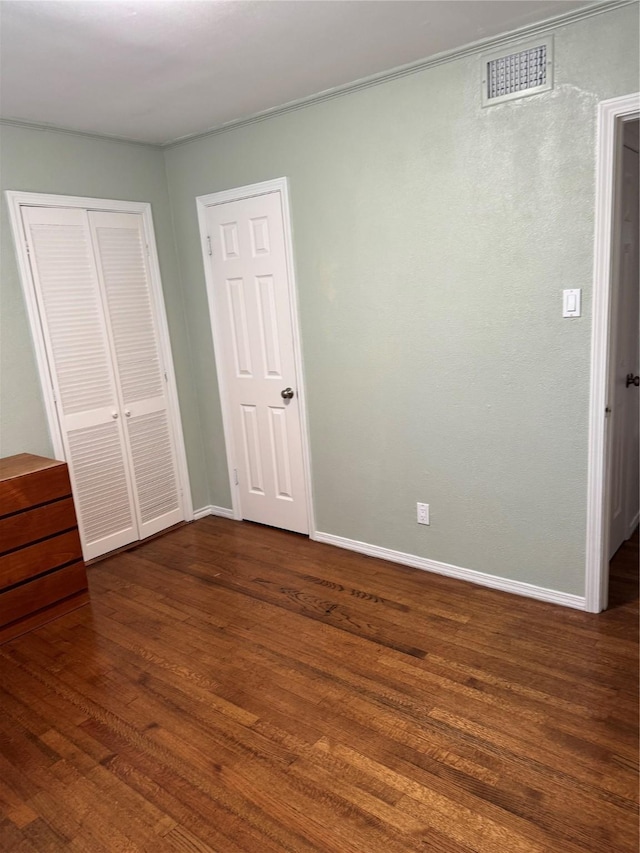 unfurnished bedroom with baseboards, visible vents, a closet, and dark wood finished floors