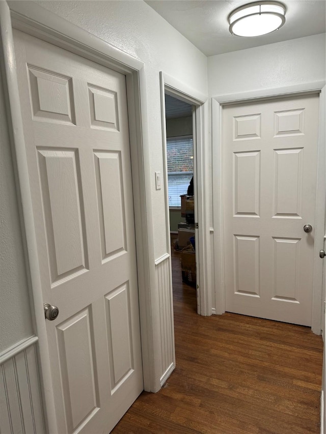 corridor with dark wood-type flooring and a textured wall