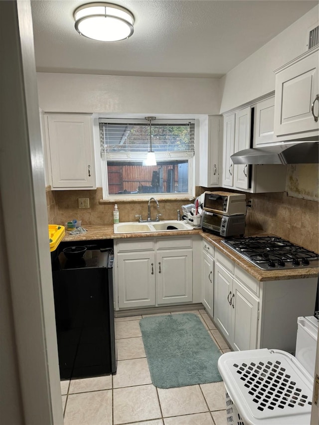 kitchen featuring light tile patterned flooring, a sink, stainless steel gas stovetop, under cabinet range hood, and white cabinets