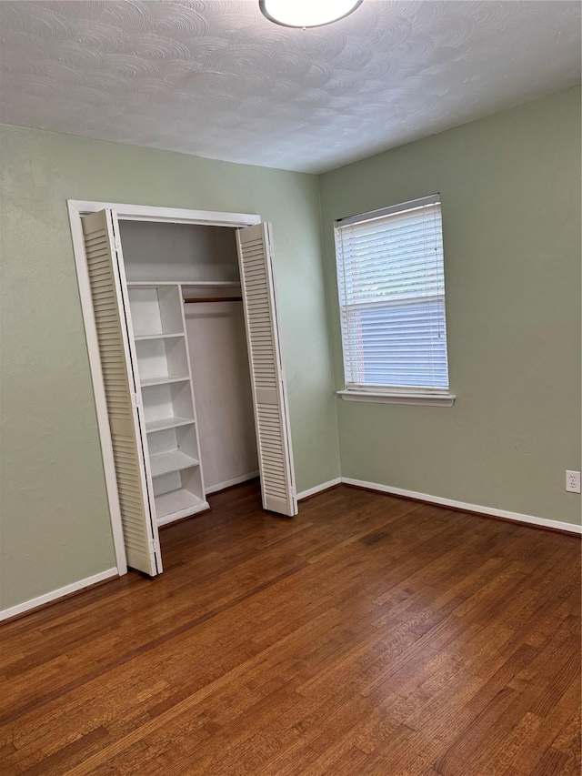 unfurnished bedroom with baseboards, a closet, and dark wood-style flooring
