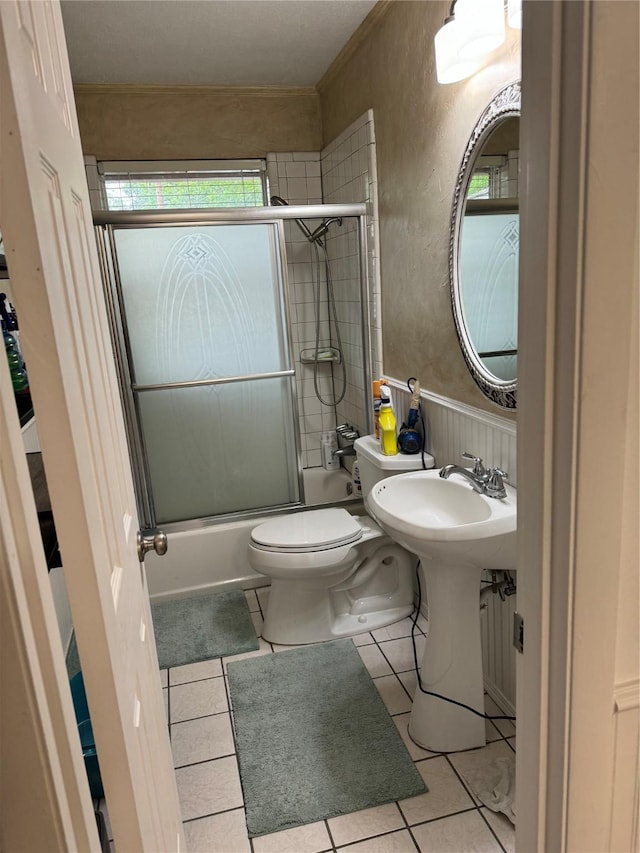full bathroom featuring toilet, tile patterned floors, a sink, a textured wall, and shower / bath combination with glass door