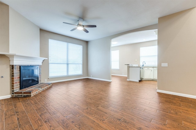 2104 Aberdeen Ave, Mckinney, TX 75072 - unfurnished living room featuring a ceiling fan, wood finished floors, arched walkways, and a brick fireplace