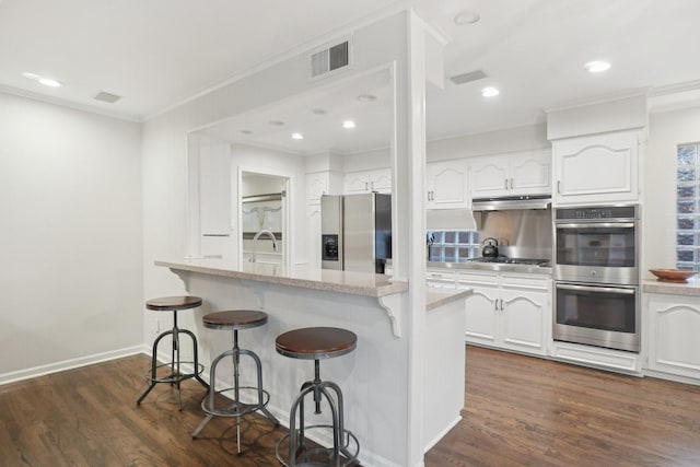3139 Citation Dr, Dallas, TX 75229 - kitchen with appliances with stainless steel finishes, under cabinet range hood, a kitchen bar, white cabinetry, and ornamental molding