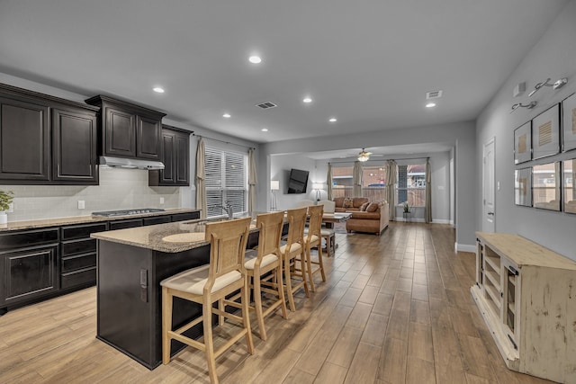 5420 Otter Trl, Fort Worth, TX 76179 - kitchen with stainless steel gas cooktop, a kitchen breakfast bar, ceiling fan, backsplash, and light wood-type flooring