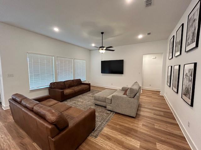 living room featuring wood finished floors, visible vents, baseboards, and ceiling fan
