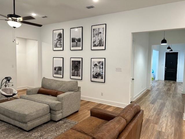 living room with baseboards, visible vents, wood finished floors, and a ceiling fan