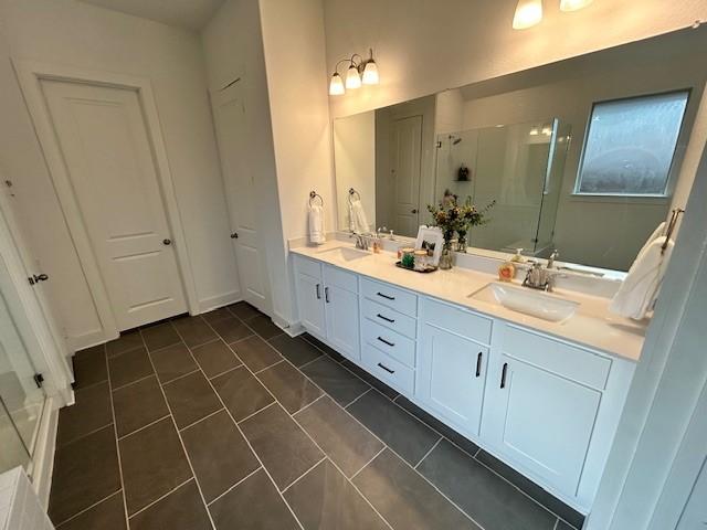 bathroom with a stall shower, double vanity, tile patterned flooring, and a sink