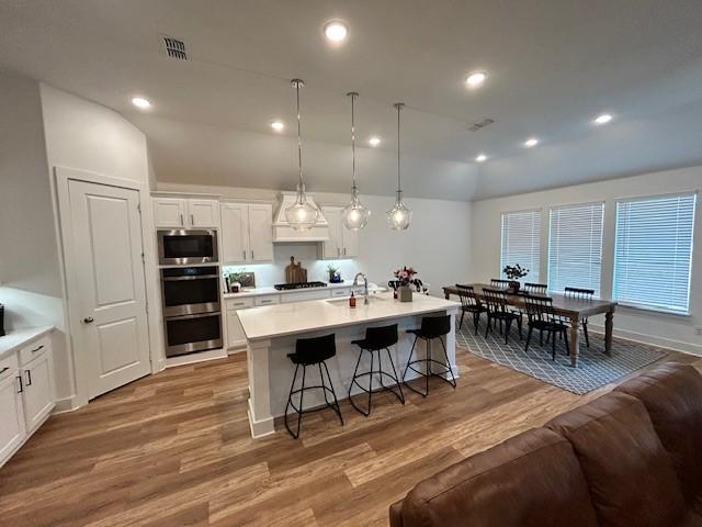 kitchen with white cabinetry, a breakfast bar area, light wood-style floors, visible vents, and appliances with stainless steel finishes