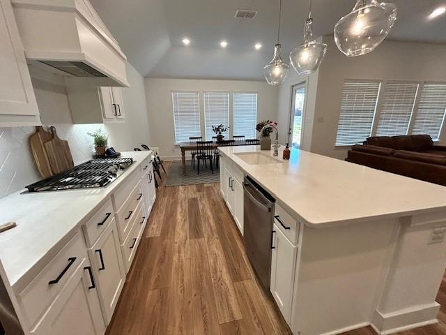 kitchen featuring light countertops, custom range hood, stainless steel appliances, a sink, and wood finished floors