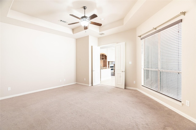 unfurnished room with a tray ceiling, a ceiling fan, baseboards, light colored carpet, and visible vents