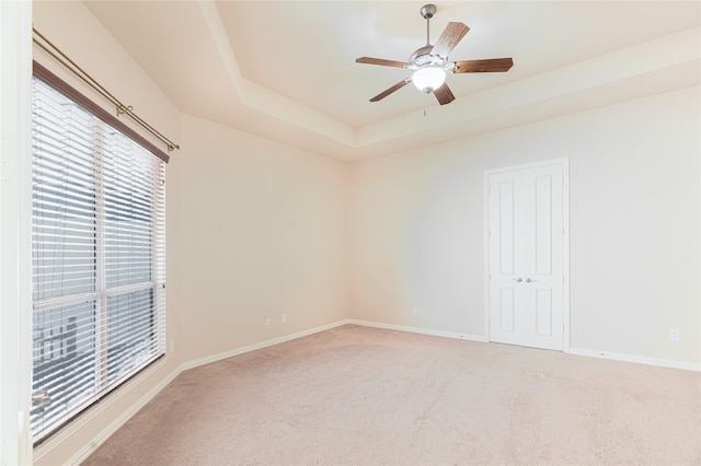 unfurnished room with light carpet, baseboards, ceiling fan, and a raised ceiling