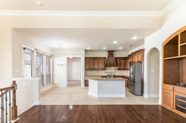 kitchen with tasteful backsplash, stainless steel refrigerator with ice dispenser, light tile patterned floors, a center island with sink, and light stone countertops