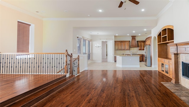 unfurnished living room with light wood-style floors, ceiling fan, ornamental molding, and a tile fireplace