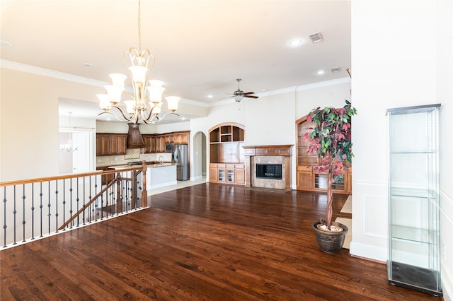 unfurnished living room with a high end fireplace, ceiling fan with notable chandelier, visible vents, ornamental molding, and dark wood-style flooring