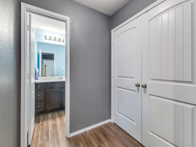 corridor with a textured wall, baseboards, wood finished floors, and a sink