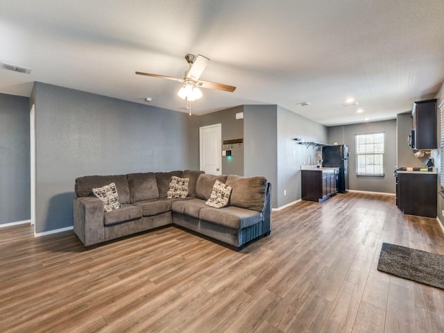 living area featuring light wood-style flooring, baseboards, ceiling fan, and visible vents