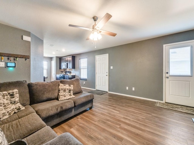 living area with a ceiling fan, baseboards, and wood finished floors