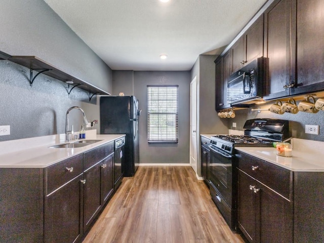 kitchen with a sink, dark brown cabinetry, light wood-style flooring, and black appliances
