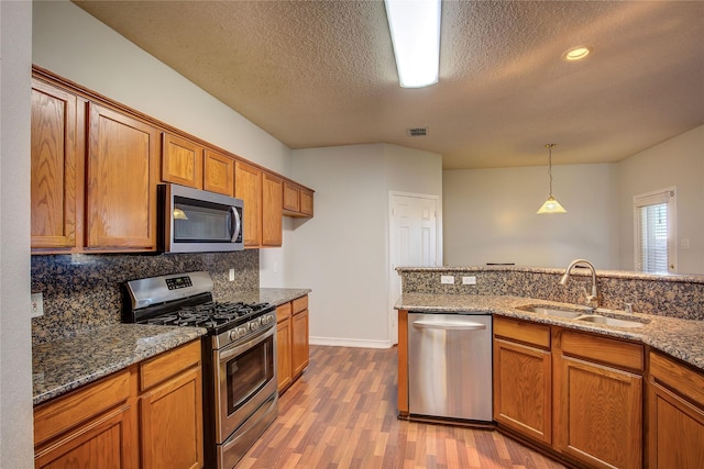 3331 Midstream Ct, Mesquite, TX 75181 - kitchen with stainless steel appliances, a sink, brown cabinetry, wood finished floors, and a textured ceiling