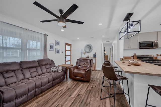 living area featuring a ceiling fan, recessed lighting, baseboards, and wood finished floors