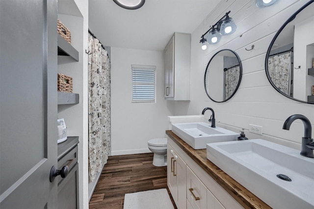 bathroom with toilet, a sink, double vanity, and wood finished floors