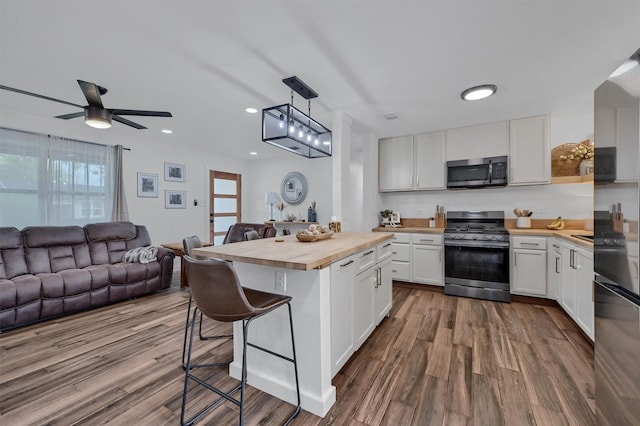 kitchen with white cabinets, stainless steel appliances, butcher block counters, open floor plan, and a breakfast bar area