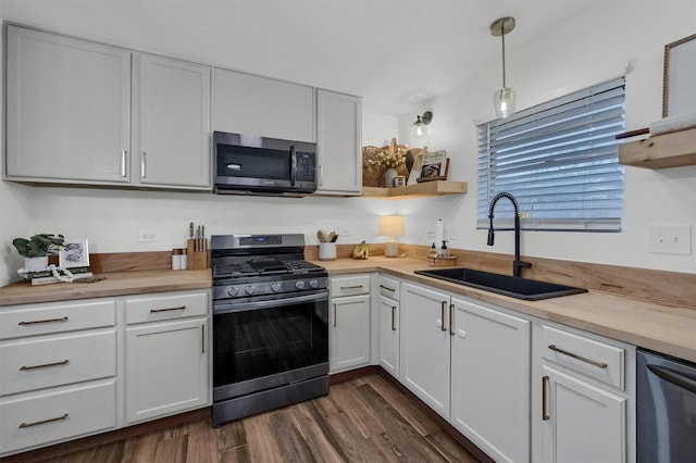 kitchen with white cabinetry, stainless steel appliances, dark wood-type flooring, a sink, and pendant lighting