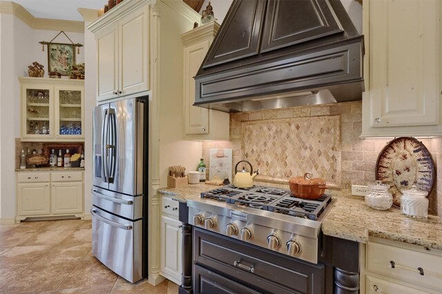 7545 Colton Ln, Pilot Point, TX 76258 - kitchen with stainless steel appliances, custom exhaust hood, decorative backsplash, light stone counters, and cream cabinetry