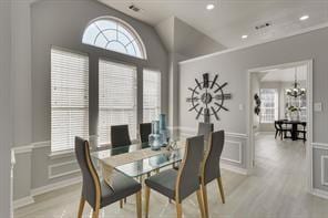 dining room featuring a chandelier, light wood-type flooring, wainscoting, a decorative wall, and lofted ceiling