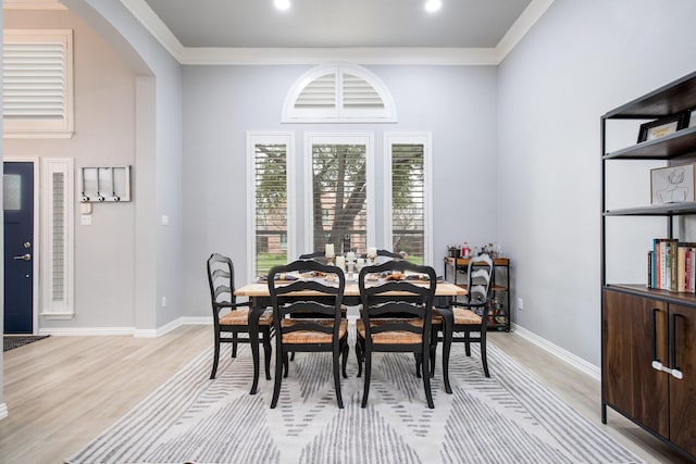 dining space featuring light wood-type flooring, crown molding, arched walkways, baseboards, and recessed lighting