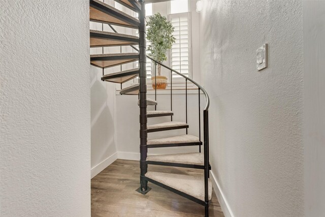 staircase featuring baseboards, a textured wall, and wood finished floors