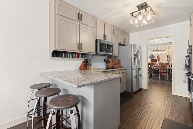 kitchen featuring a kitchen breakfast bar, stainless steel appliances, dark wood-style floors, light stone counters, and a peninsula