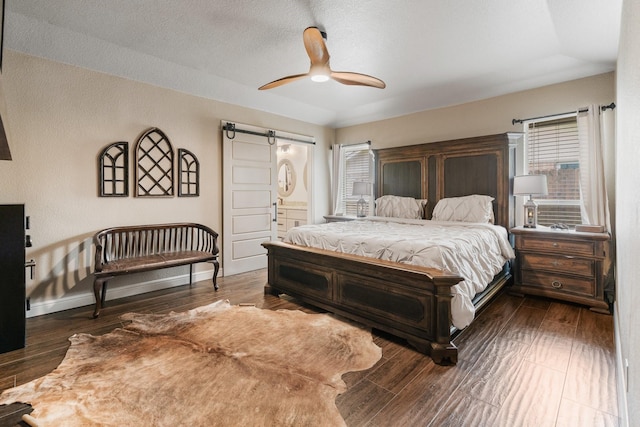 bedroom with connected bathroom, baseboards, a barn door, and dark wood-style flooring
