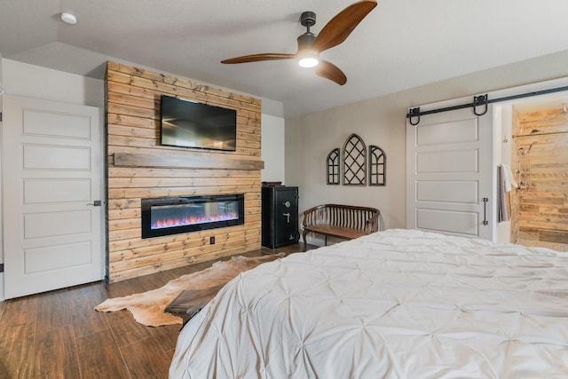 bedroom featuring a barn door, a glass covered fireplace, ensuite bathroom, ceiling fan, and dark wood-type flooring