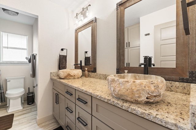 bathroom featuring double vanity, a sink, toilet, and wood finished floors